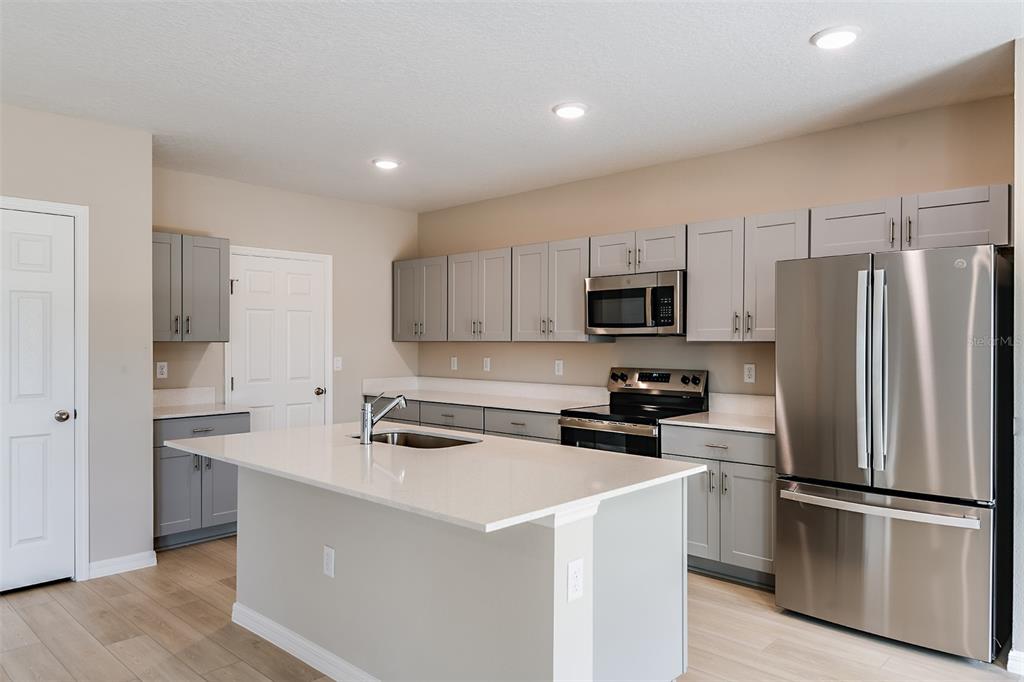 A modern kitchen features gray cabinets, white countertops, a central island, and stainless steel appliances — 9110 BELLEVIEW FOREST PASS, DADE CITY, FL