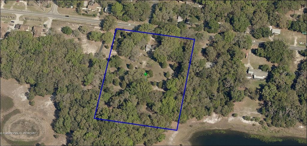 An aerial view shows a wooded residential lot outlined in blue next to a lake — 2048 MILLER BOULEVARD, FRUITLAND PARK, FL