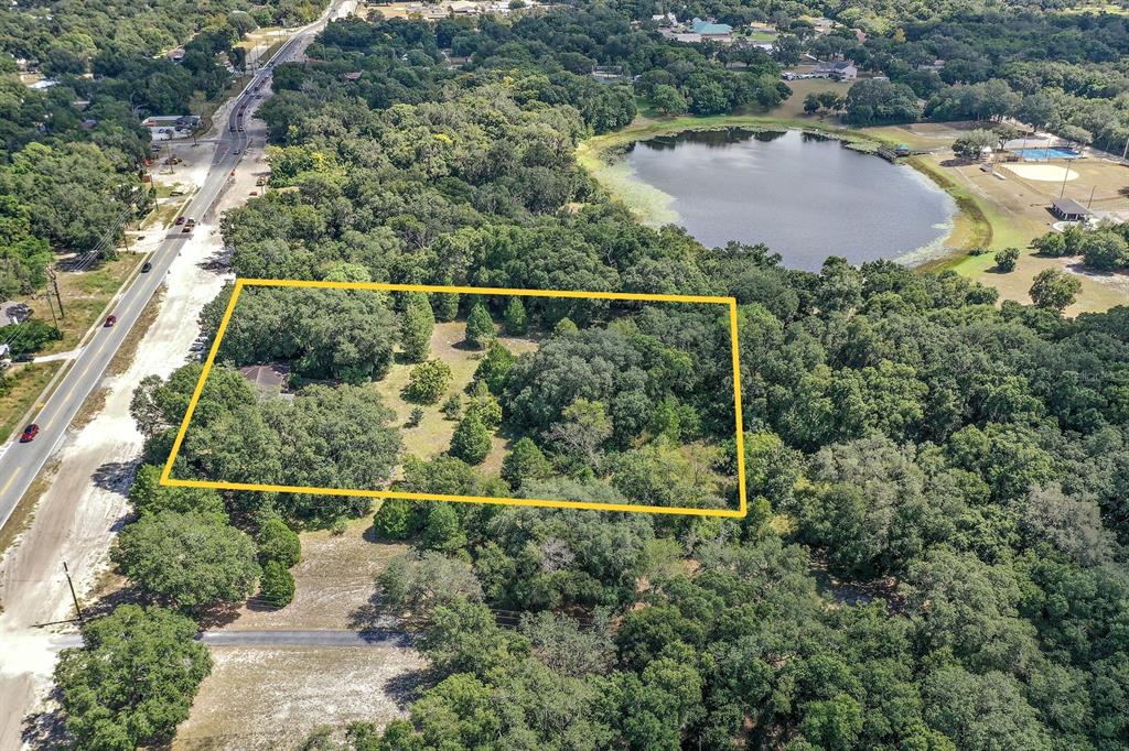 An aerial view shows a wooded lot outlined in yellow near a road and lake — 2048 MILLER BOULEVARD, FRUITLAND PARK, FL