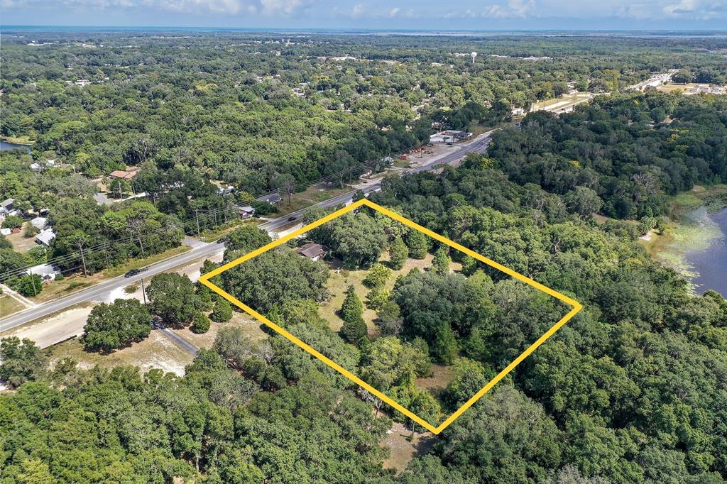 An aerial view shows a wooded lot outlined in yellow next to a paved road — 2048 MILLER BOULEVARD, FRUITLAND PARK, FL
