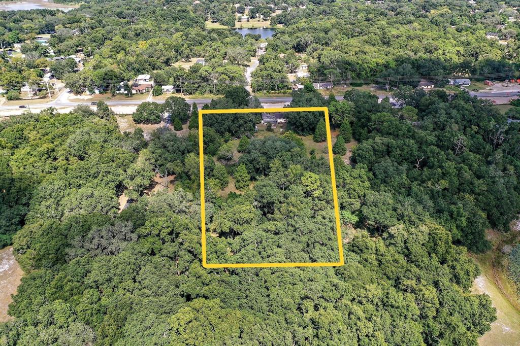 An aerial view shows a rectangular plot of land outlined in yellow amidst dense trees — 2048 MILLER BOULEVARD, FRUITLAND PARK, FL