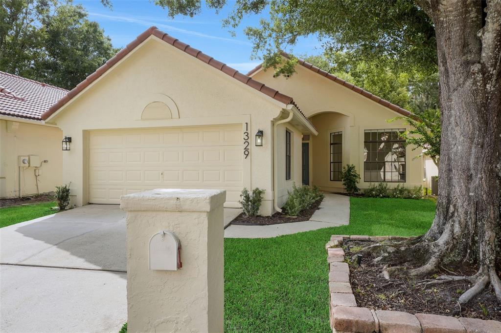 A single-story house with a beige stucco exterior, a tile roof, and a concrete driveway — 1329 AUGUSTA NATIONAL BOULEVARD, WINTER SPRINGS, FL