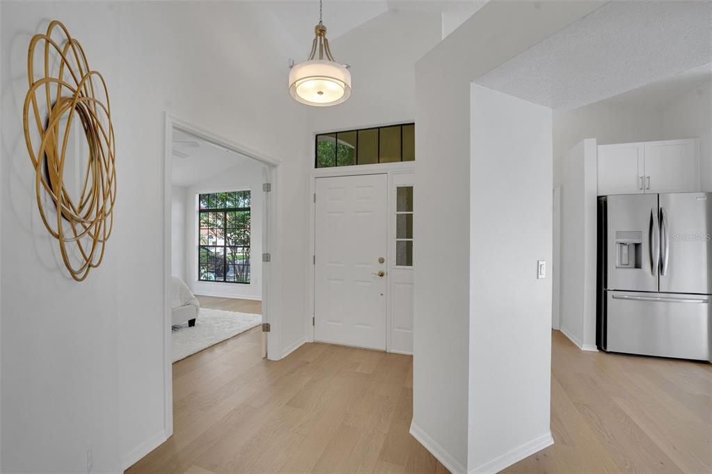 An entryway with light wood flooring, a white front door, and a view into a bedroom — 1329 AUGUSTA NATIONAL BOULEVARD, WINTER SPRINGS, FL