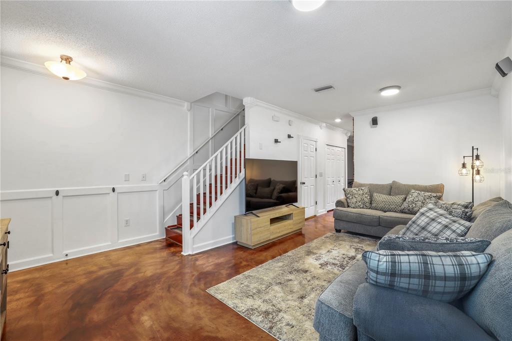 A living room features stained concrete floors, white wainscoting, a staircase, and gray furniture — 6130 OSPREY LAKE CIRCLE, RIVERVIEW, FL