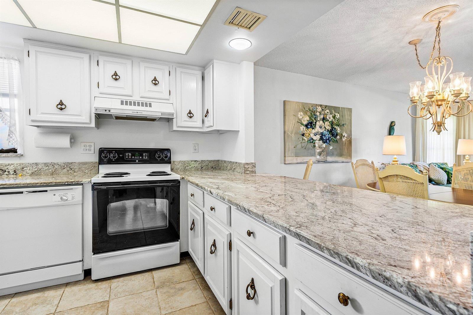 A kitchen with white cabinets, granite countertops, and a black oven, opening to a dining area — 4085 Kittiwake Court, Boynton Beach FL 33436, BOYNTON BEACH, FL