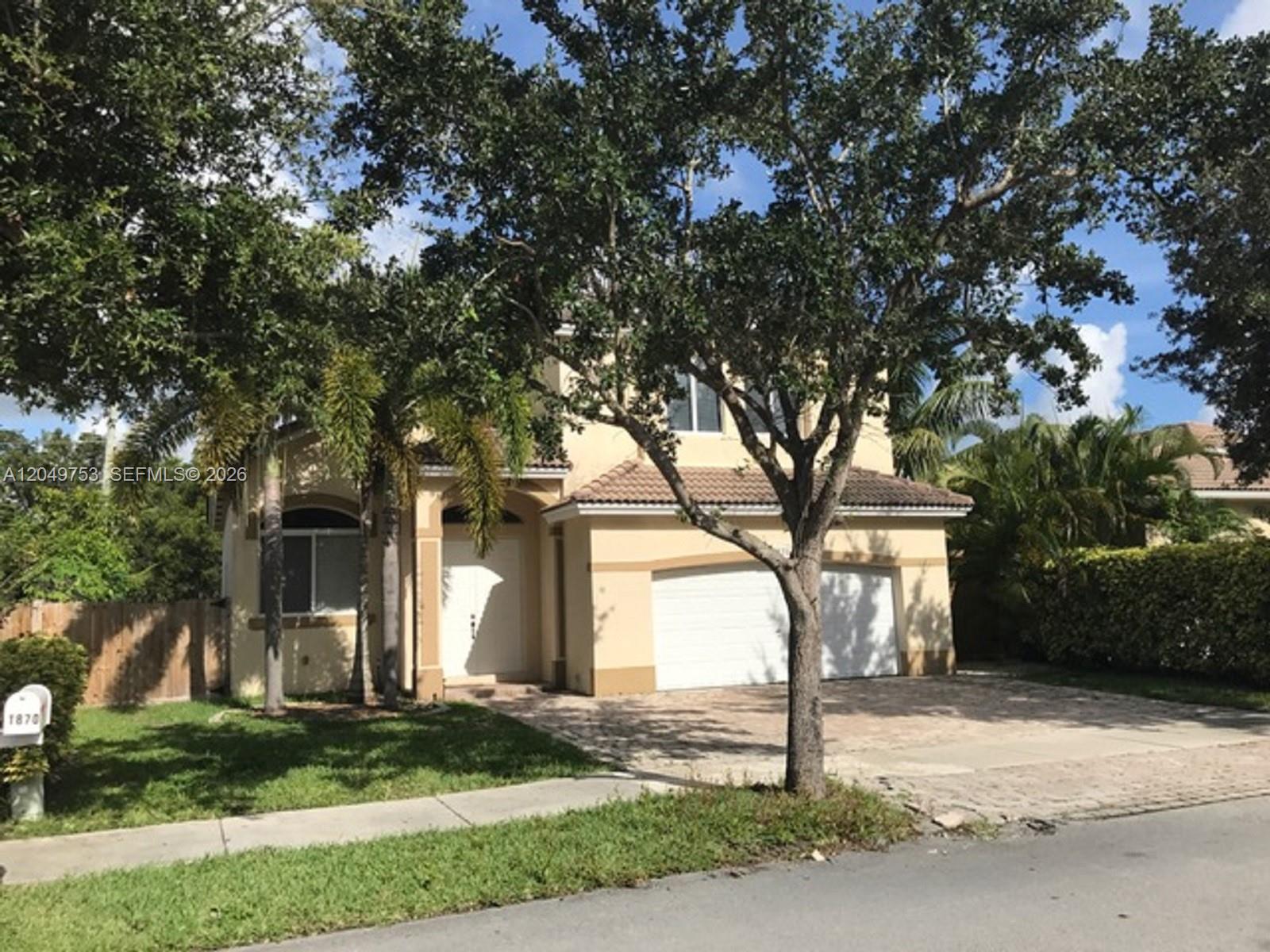 A two-story tan house with a two-car garage and a large tree in front — 1870 SE 18th Ter, Homestead FL 33035, HOMESTEAD, FL
