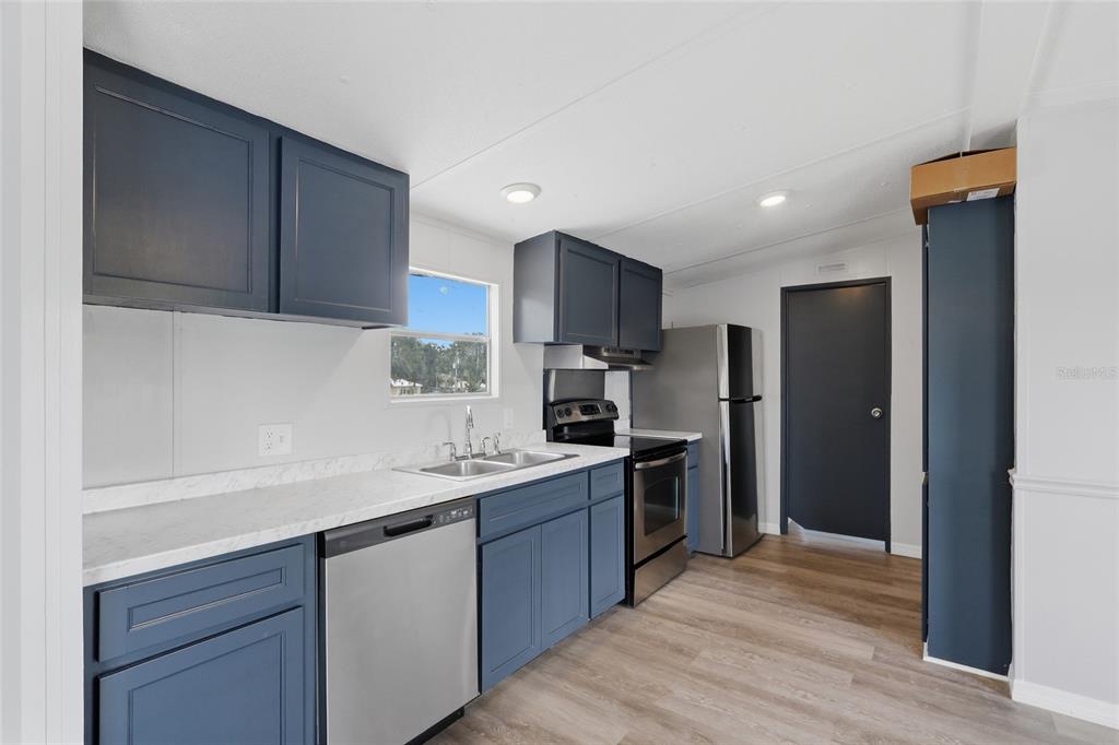 A kitchen features blue cabinets, stainless steel appliances, and white countertops with a marble pattern — 7930 FROGGY LANE, ZEPHYRHILLS, FL