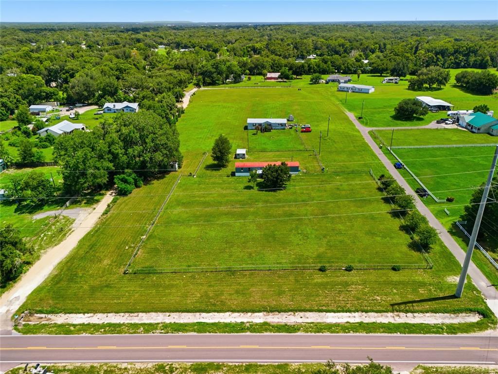 An aerial view shows a fenced grassy lot with two houses and a road — 7930 FROGGY LANE, ZEPHYRHILLS, FL