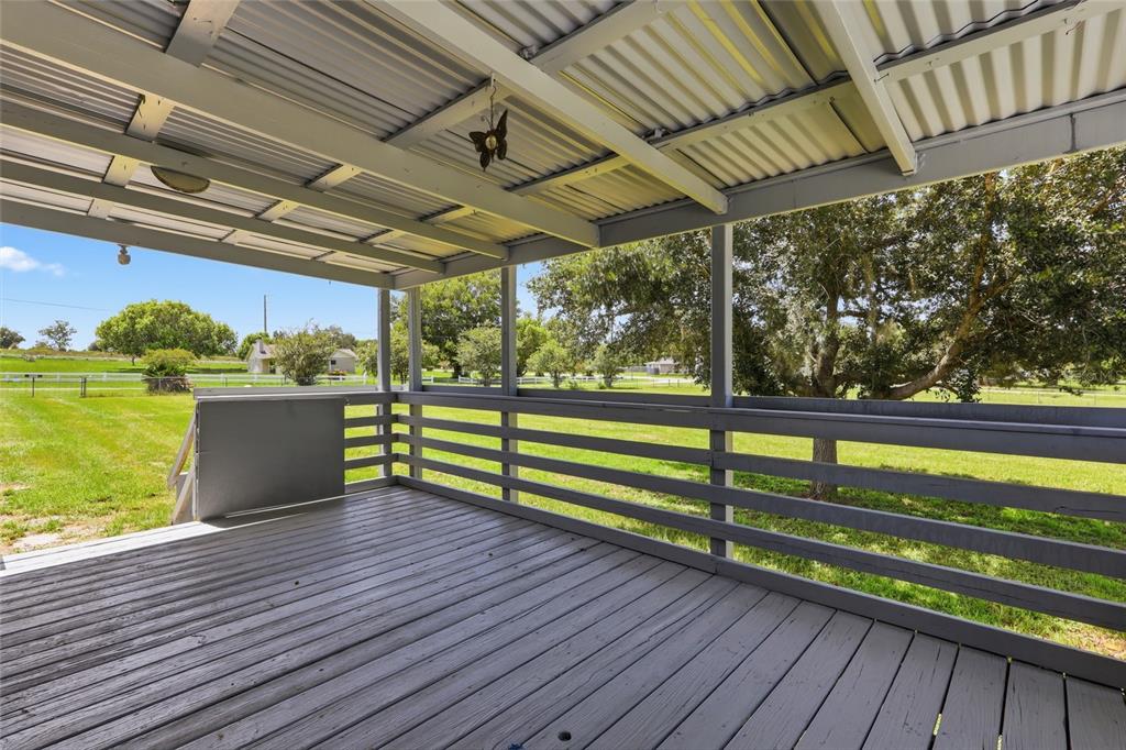 A covered wooden deck overlooks a grassy yard with trees and a white fence — 7930 FROGGY LANE, ZEPHYRHILLS, FL