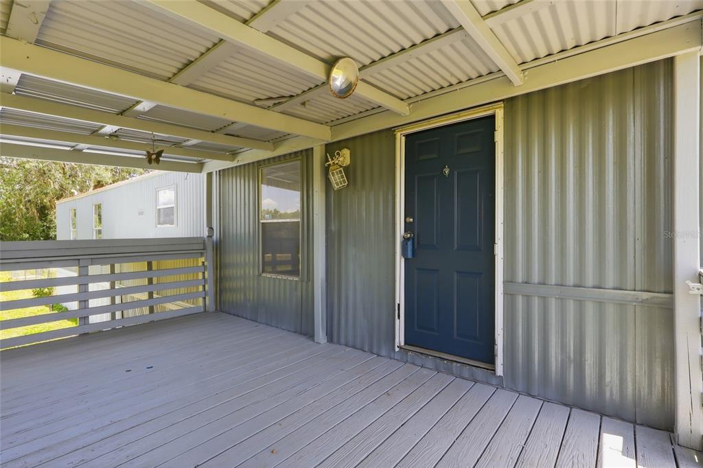 A covered wooden porch features a blue front door and corrugated metal exterior walls — 7930 FROGGY LANE, ZEPHYRHILLS, FL