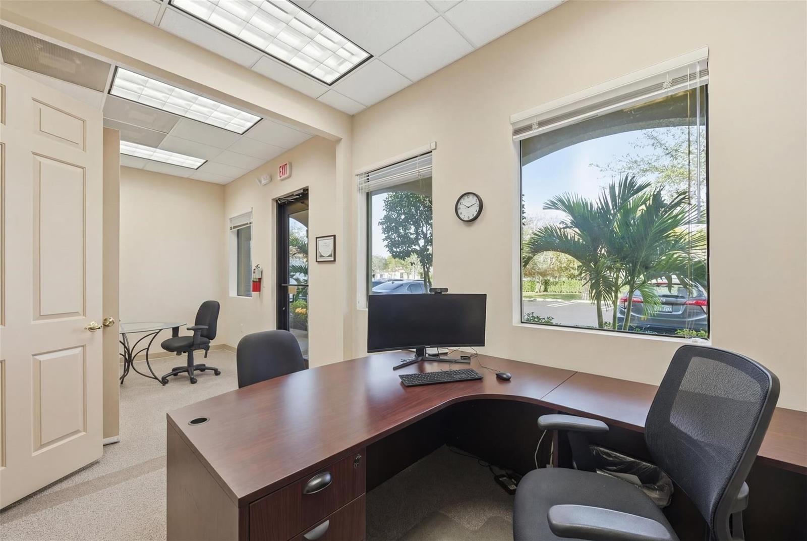 An office space features a dark wood L-shaped desk, two chairs, and large windows — CORAL SPRINGS, FL