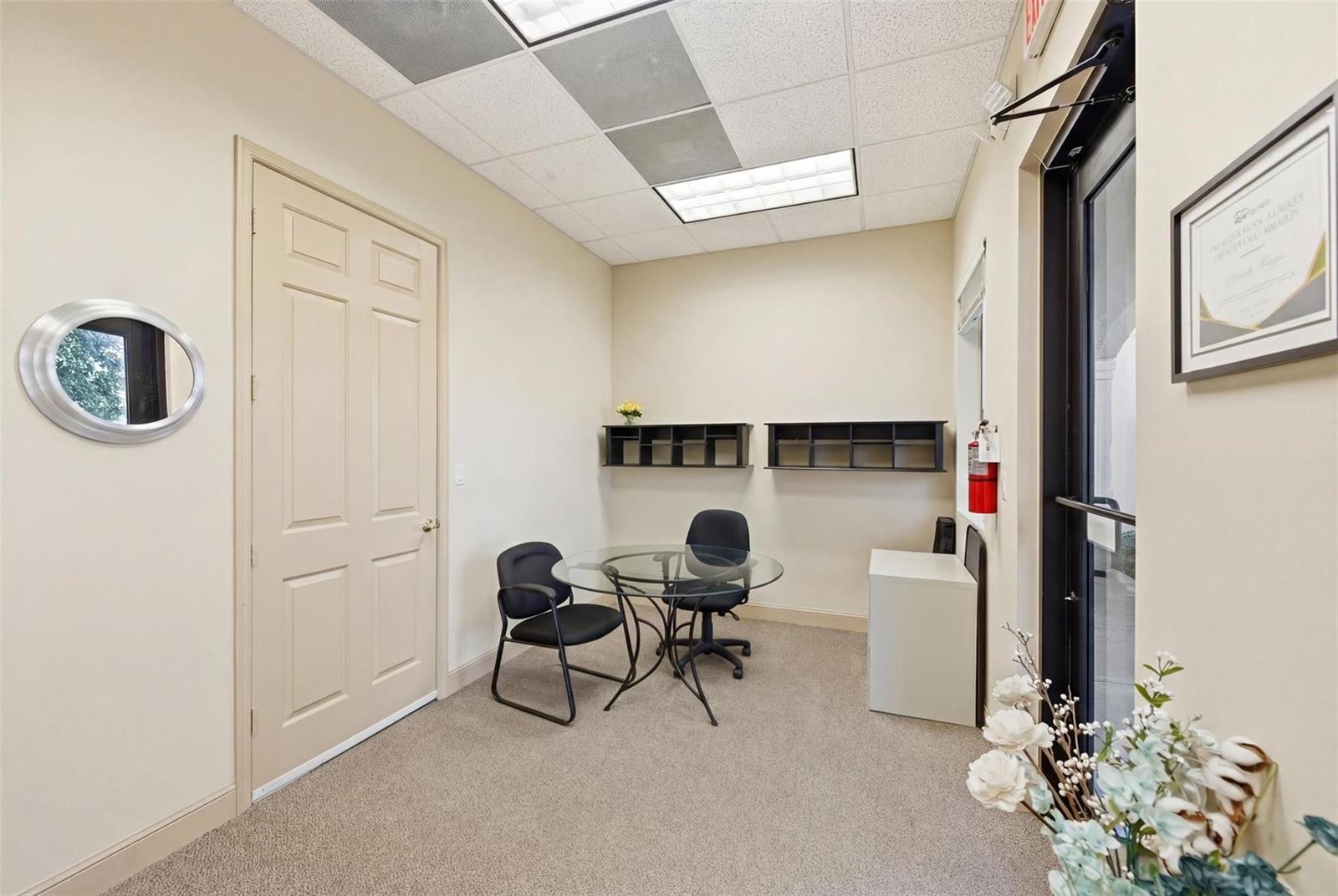 A small office features a glass table, two chairs, wall-mounted shelving, and a glass door — CORAL SPRINGS, FL