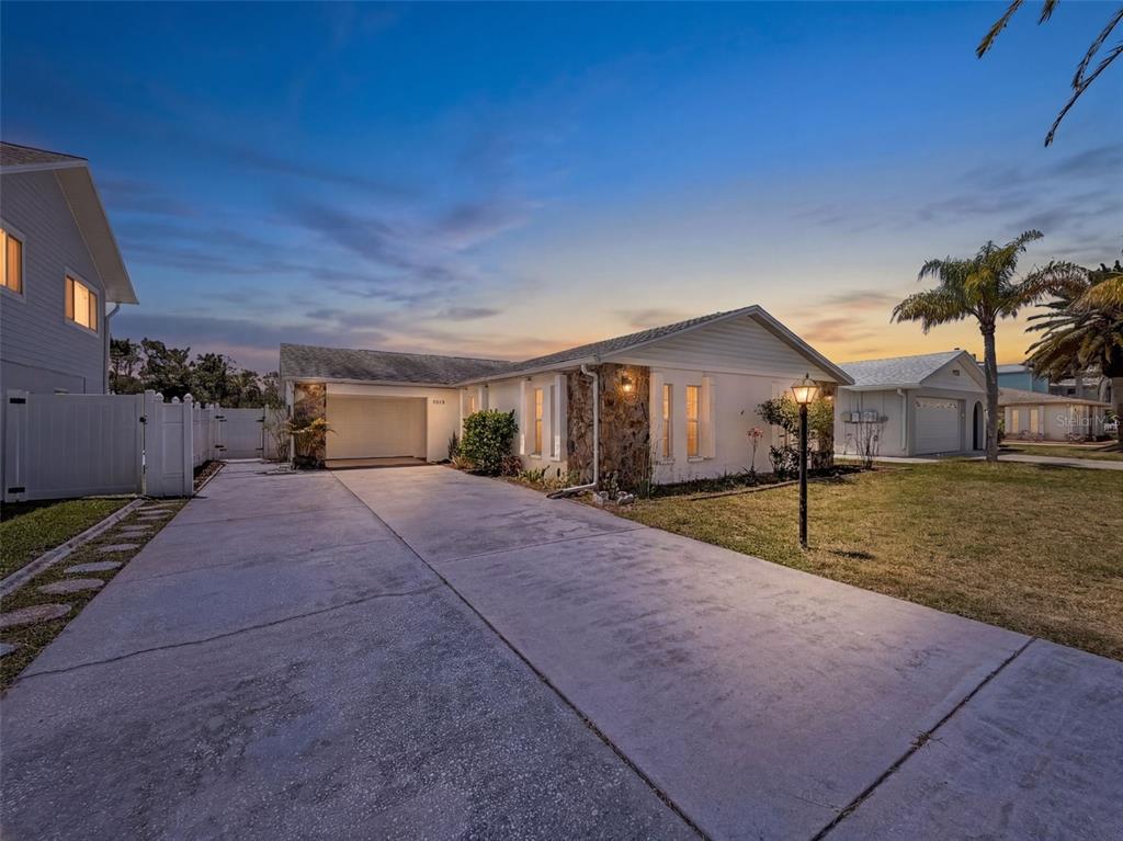 A single-story house with a stone facade and a concrete driveway at sunset — 7038 SOUTHWIND DRIVE, HUDSON, FL