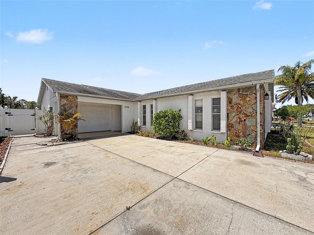 A single-story house with a white stucco exterior, stone accents, and a concrete driveway — 7038 SOUTHWIND DRIVE, HUDSON, FL
