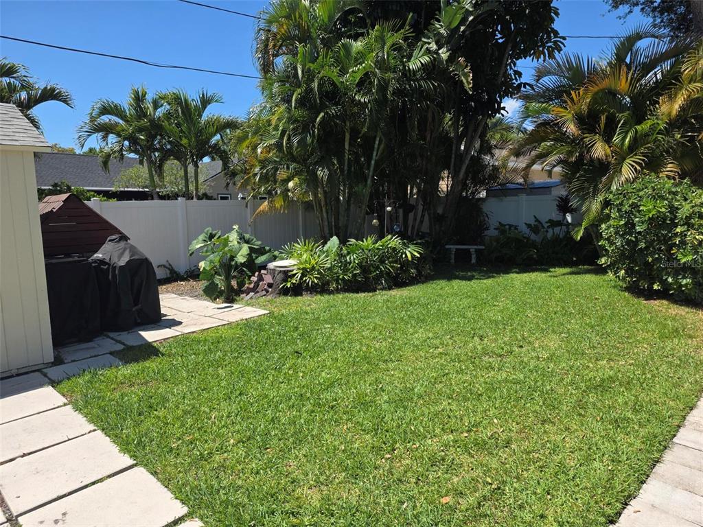 A backyard features a green lawn, palm trees, a white fence, and a paved patio — 734 37TH AVENUE N, ST PETERSBURG, FL