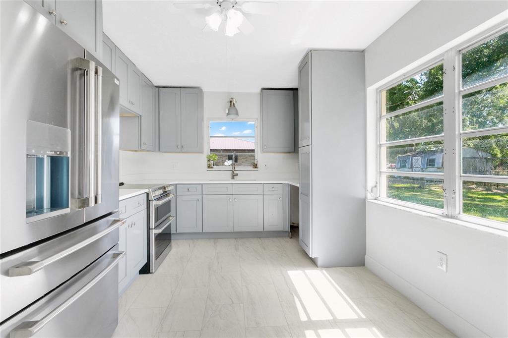 A kitchen features gray cabinets, stainless steel appliances, white countertops, and a large side window — 1801 EASTERN AVENUE, ST CLOUD, FL