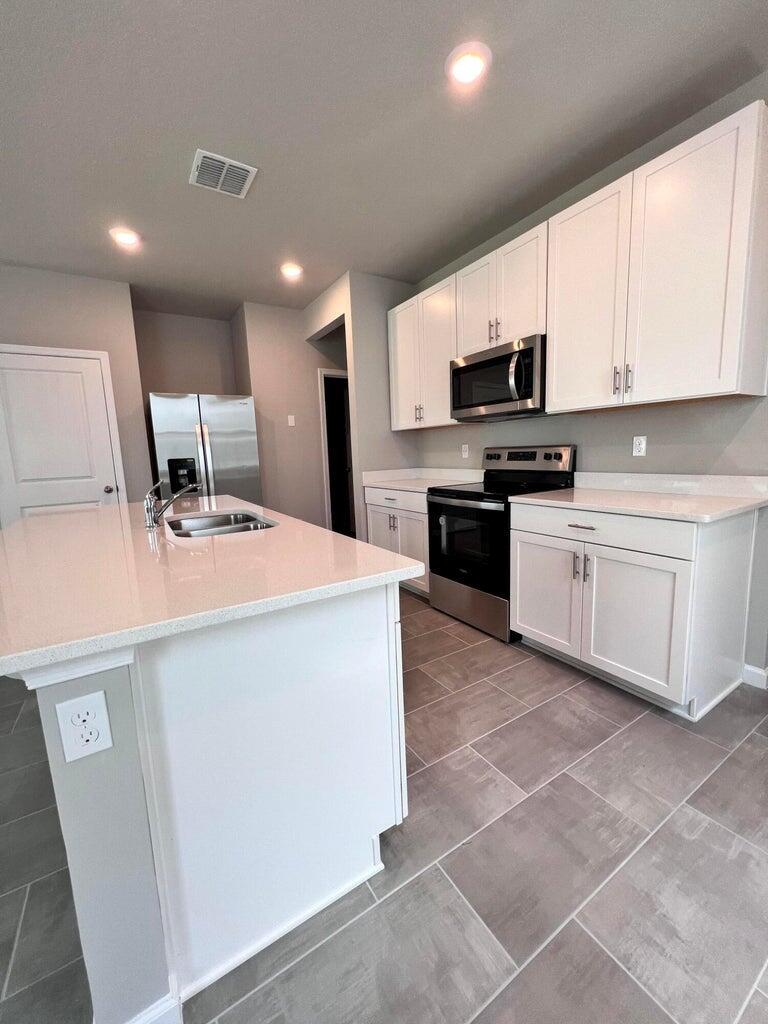 A modern kitchen features white cabinets, stainless steel appliances, a quartz island, and tile flooring — 254 Osprey Preserve Boulevard, Jensen Beach FL 34957, JENSEN BEACH, FL