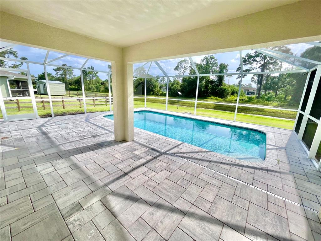 A covered patio with paver flooring overlooks a rectangular swimming pool enclosed by a screen — 5029 W HUMMINGBIRD DRIVE, LABELLE, FL