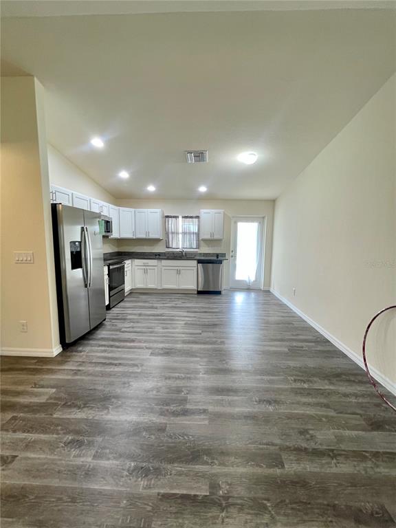 An open-concept kitchen features white cabinets, stainless steel appliances, and wood-look flooring — 5029 W HUMMINGBIRD DRIVE, LABELLE, FL