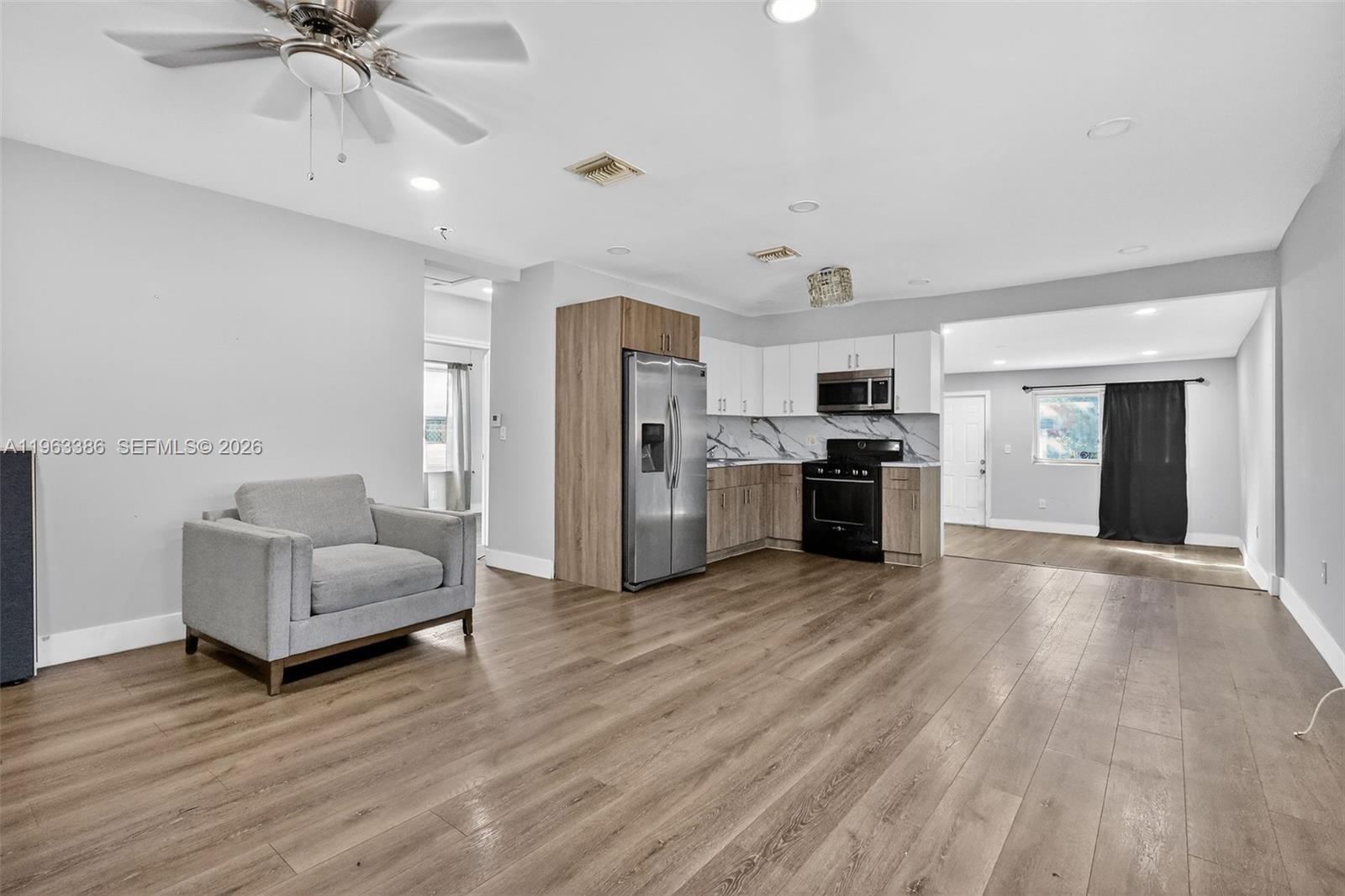 An open-concept living area features wood-look flooring, a gray armchair, and a modern kitchen — 1880 NW 69th St, Miami FL 33147, MIAMI, FL