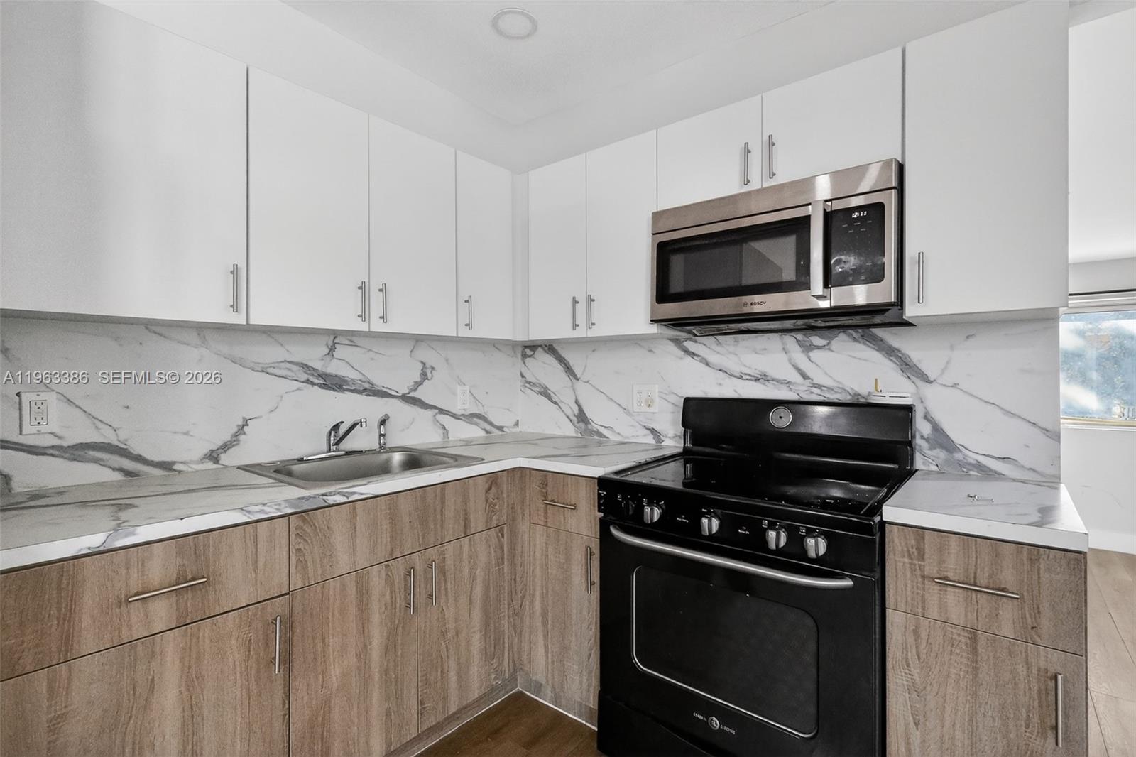 A kitchen features white upper cabinets, wood-tone lower cabinets, a black stove, and marble-patterned countertops — 1880 NW 69th St, Miami FL 33147, MIAMI, FL