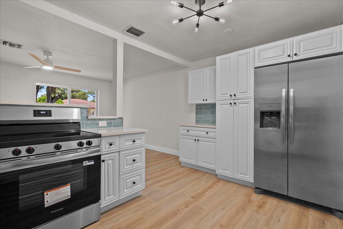 A kitchen features white cabinets, stainless steel appliances, and light wood-look flooring — 1414 S N Street, FL 33460, FL