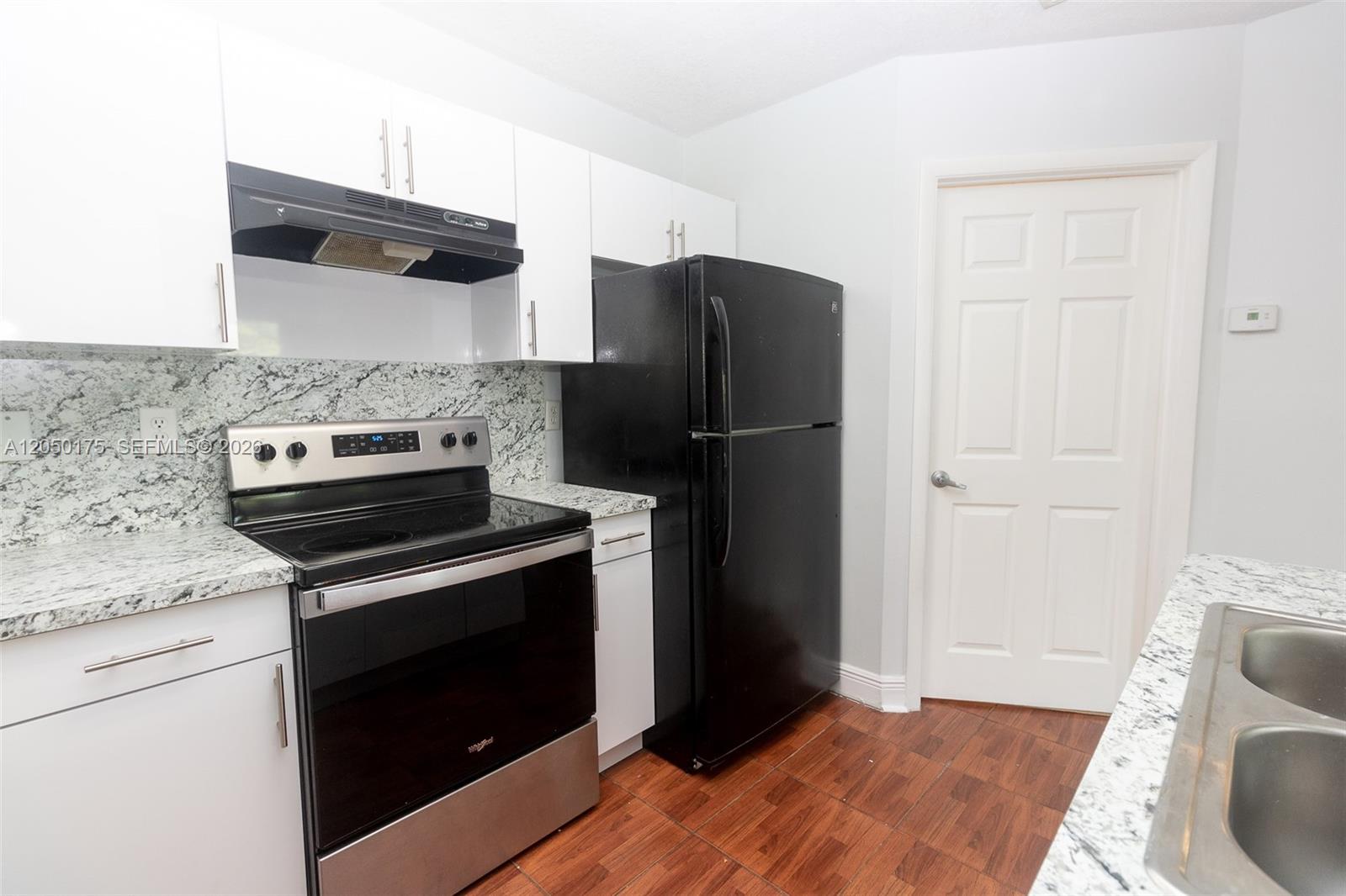 A kitchen features white cabinets, granite countertops, a black refrigerator, and a stainless steel stove — 18308 NW 68th Ave # L, Hialeah FL 33015, HIALEAH, FL
