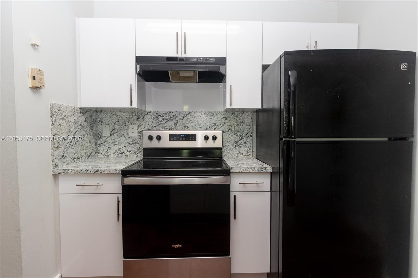 A kitchen features white cabinets, granite countertops, a black refrigerator, and a stainless steel stove — 18308 NW 68th Ave # L, Hialeah FL 33015, HIALEAH, FL