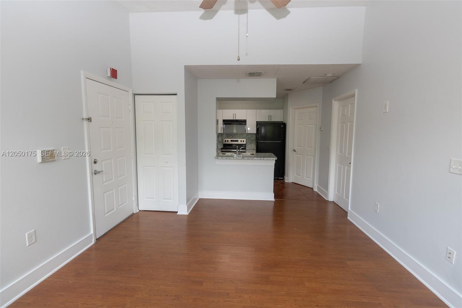 This room features wood-look flooring, white walls, and an open kitchen with black appliances — 18308 NW 68th Ave # L, Hialeah FL 33015, HIALEAH, FL