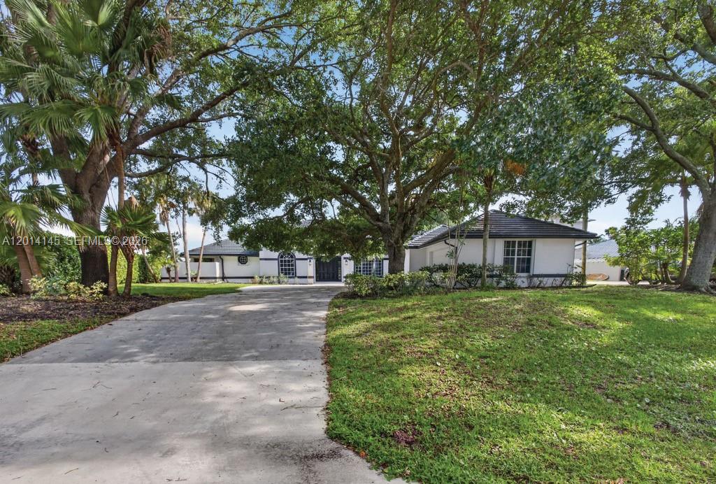 A white single-story house with a concrete driveway sits under large shade trees — 19558 Red Gum Trl, Jupiter FL 33458, JUPITER, FL