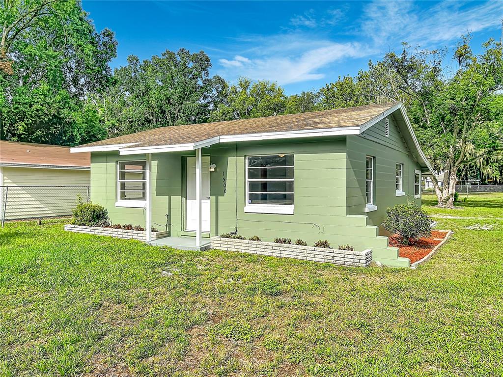 A single-story green house with a white front door and a brick planter box — 1500 S SUMMERLIN AVENUE, SANFORD, FL