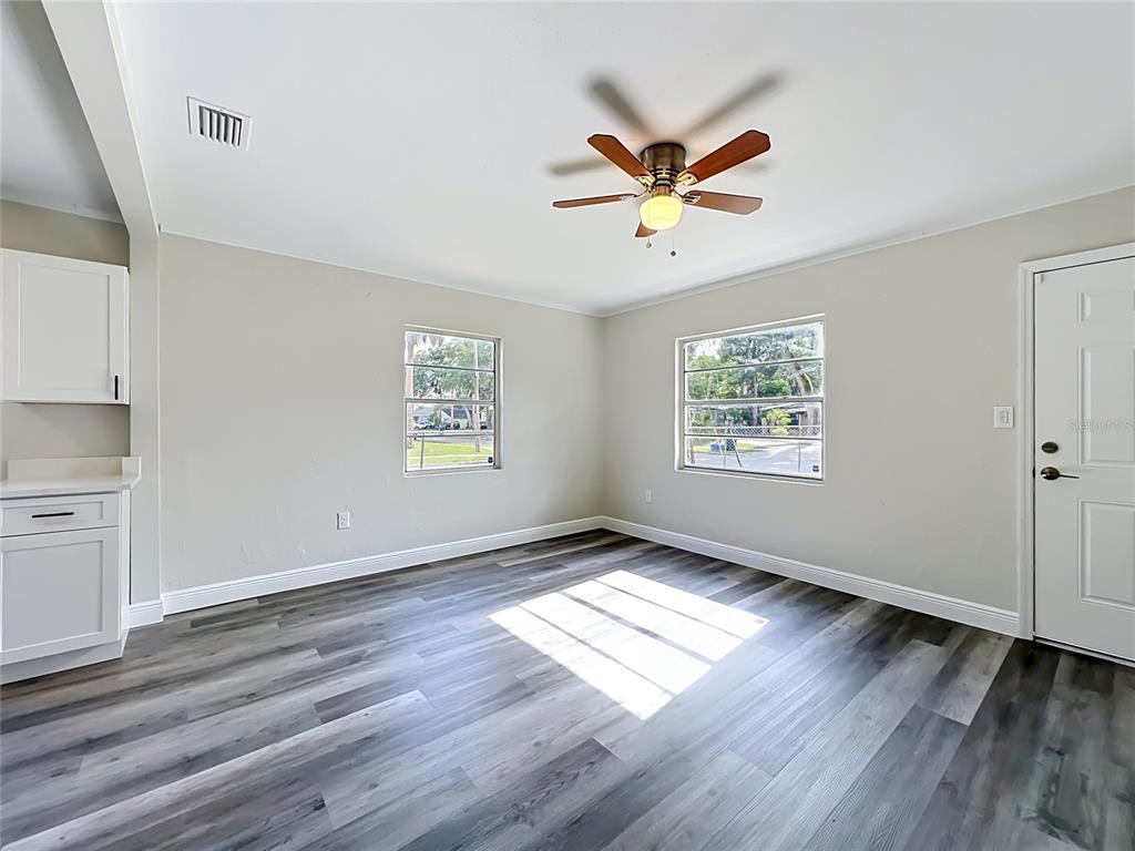 A bright room features gray wood-look flooring, white walls, two windows, and a ceiling fan — 1500 S SUMMERLIN AVENUE, SANFORD, FL