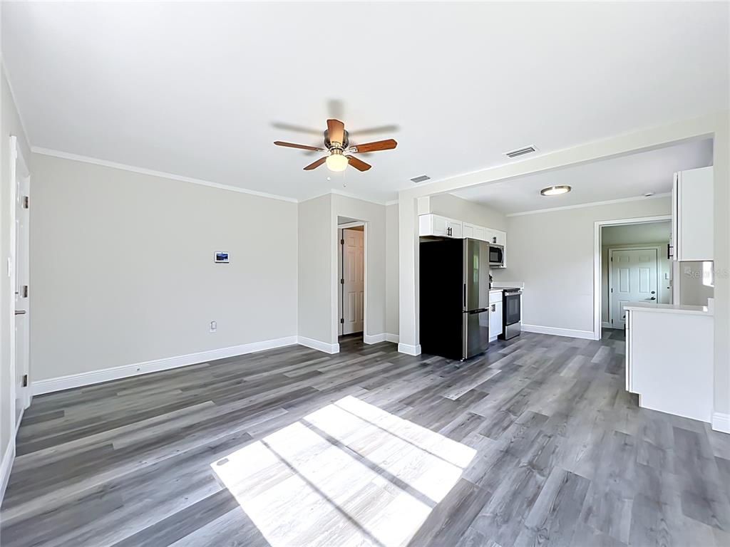 A living room with gray wood-look flooring opens into a kitchen with stainless steel appliances — 1500 S SUMMERLIN AVENUE, SANFORD, FL