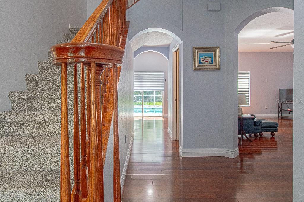 A staircase with a wooden railing leads to a hallway with hardwood floors and arches — 1745 OAK POND COURT, OLDSMAR, FL
