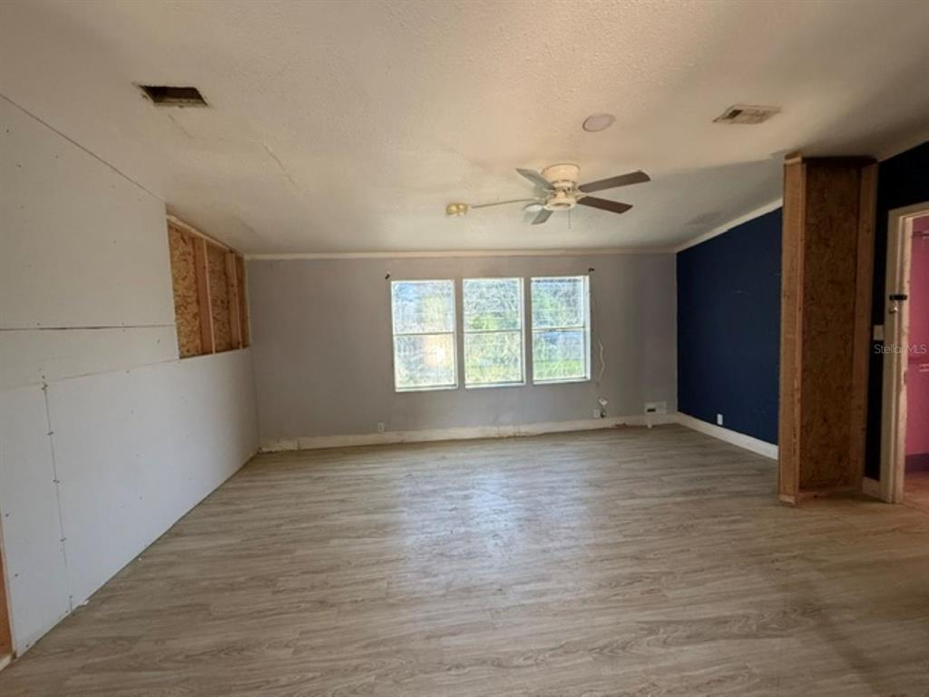An unfinished living room features light wood-look flooring, a ceiling fan, and exposed wall studs — 11881 RANCHO DRIVE, LEESBURG, FL