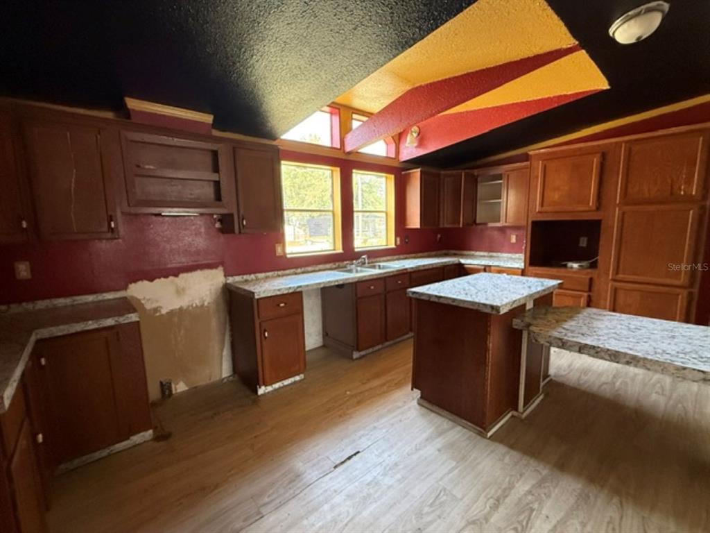 A kitchen with wood cabinets, granite-look countertops, red walls, and a vaulted ceiling — 11881 RANCHO DRIVE, LEESBURG, FL