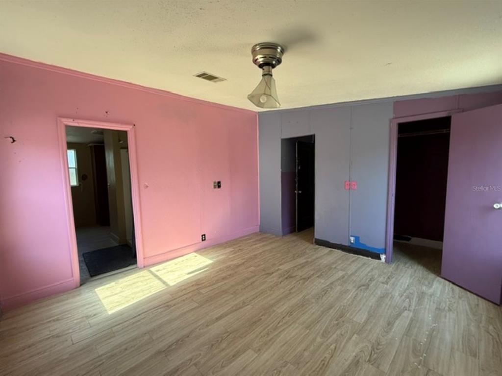 A bedroom features pink and purple walls, wood-look flooring, and a ceiling light fixture — 11881 RANCHO DRIVE, LEESBURG, FL