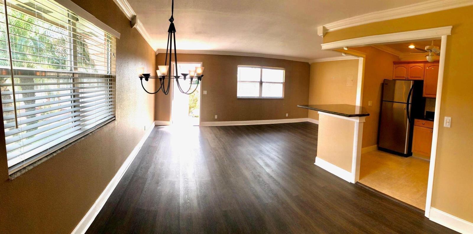 An open-concept living area with dark wood-look flooring, a chandelier, and an adjacent kitchen — 163 Waterford G, Delray Beach FL 33446, DELRAY BEACH, FL