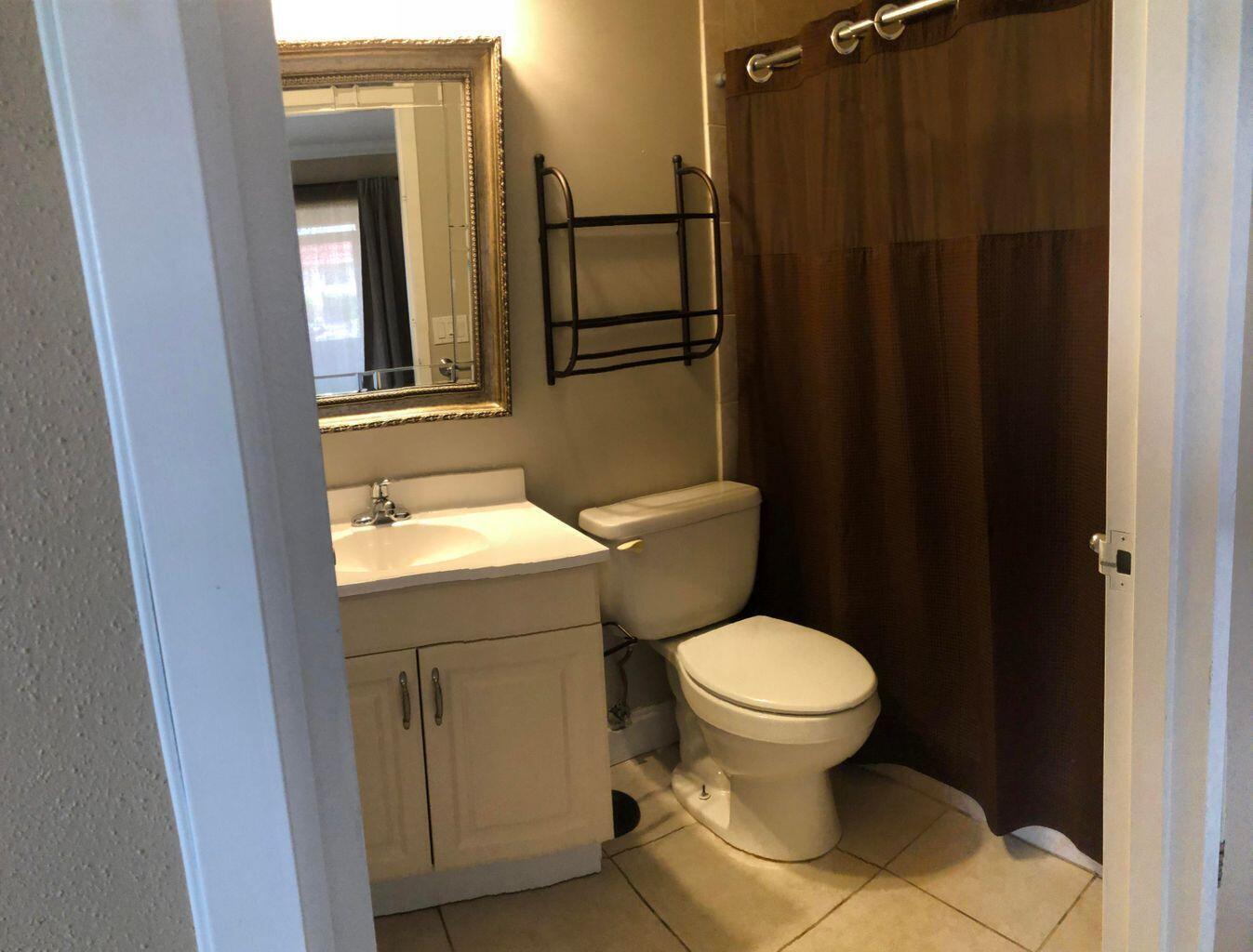 A bathroom features a white vanity, a toilet, a gold-framed mirror, and a brown shower curtain — 163 Waterford G, Delray Beach FL 33446, DELRAY BEACH, FL