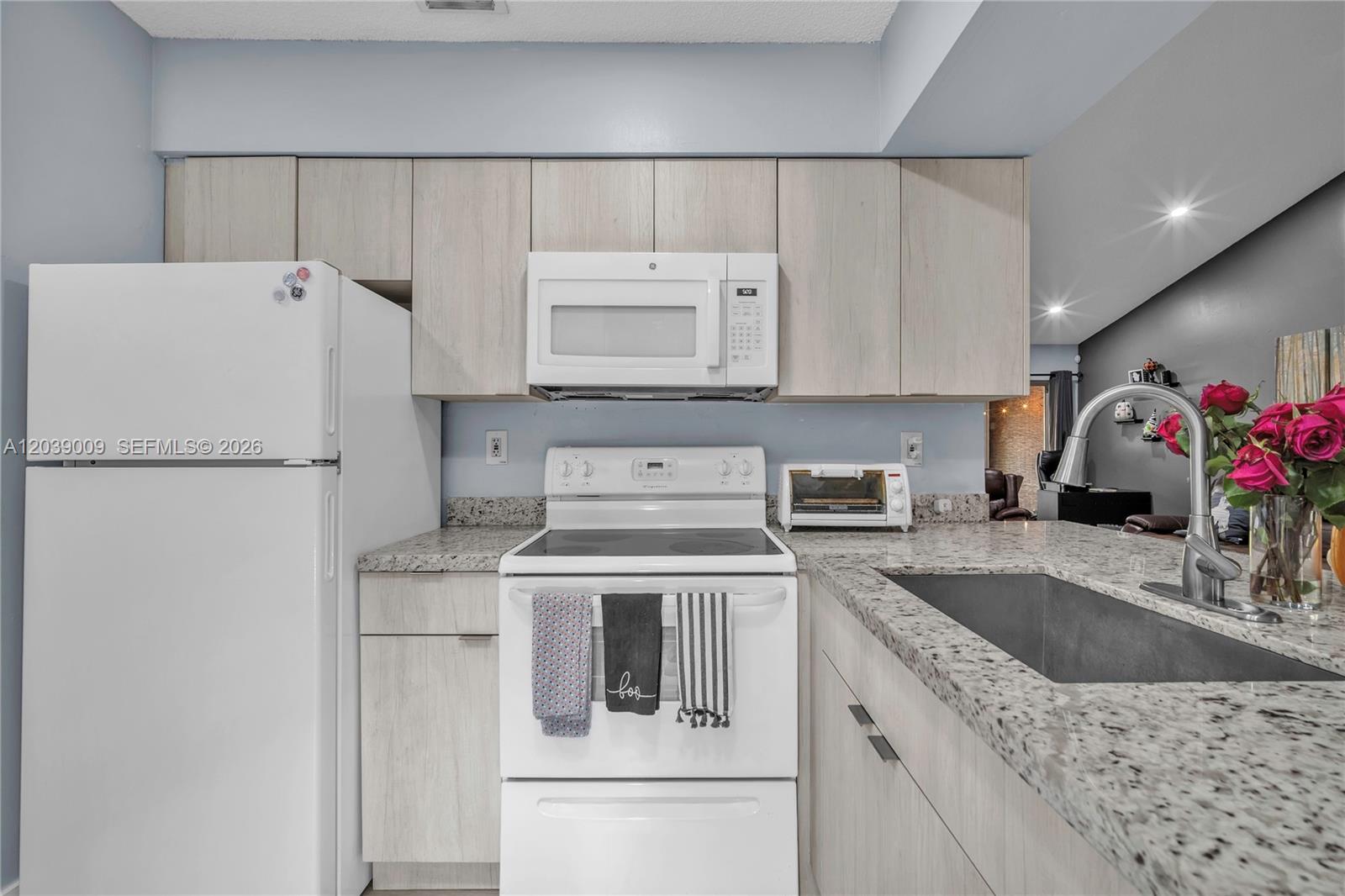 A kitchen features light wood cabinets, white appliances, granite countertops, and a stainless steel sink — 9507 SW 140th Ct # 9507, Miami FL 33186, MIAMI, FL