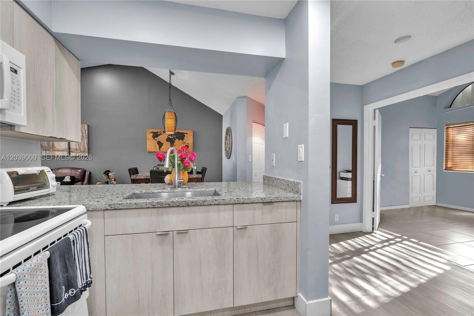 A kitchen with light wood cabinets and granite countertops overlooks a dining area — 9507 SW 140th Ct # 9507, Miami FL 33186, MIAMI, FL