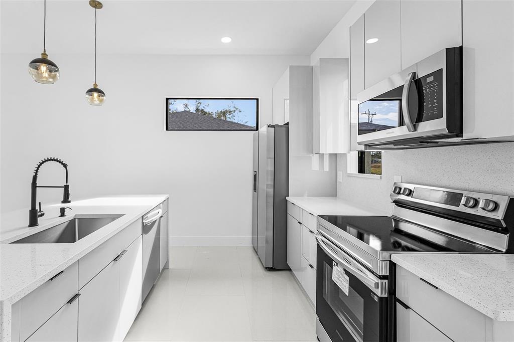 A modern kitchen features white cabinets, stainless steel appliances, and a quartz-topped island — 918 ANACONDA AVENUE S, LEHIGH ACRES, FL