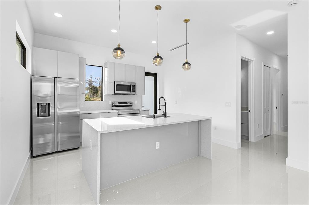 A modern kitchen features white cabinetry, stainless steel appliances, and a central quartz island — 918 ANACONDA AVENUE S, LEHIGH ACRES, FL