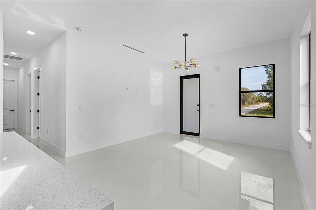 A bright, modern dining area features white walls, glossy tile floors, and a contemporary chandelier — 918 ANACONDA AVENUE S, LEHIGH ACRES, FL