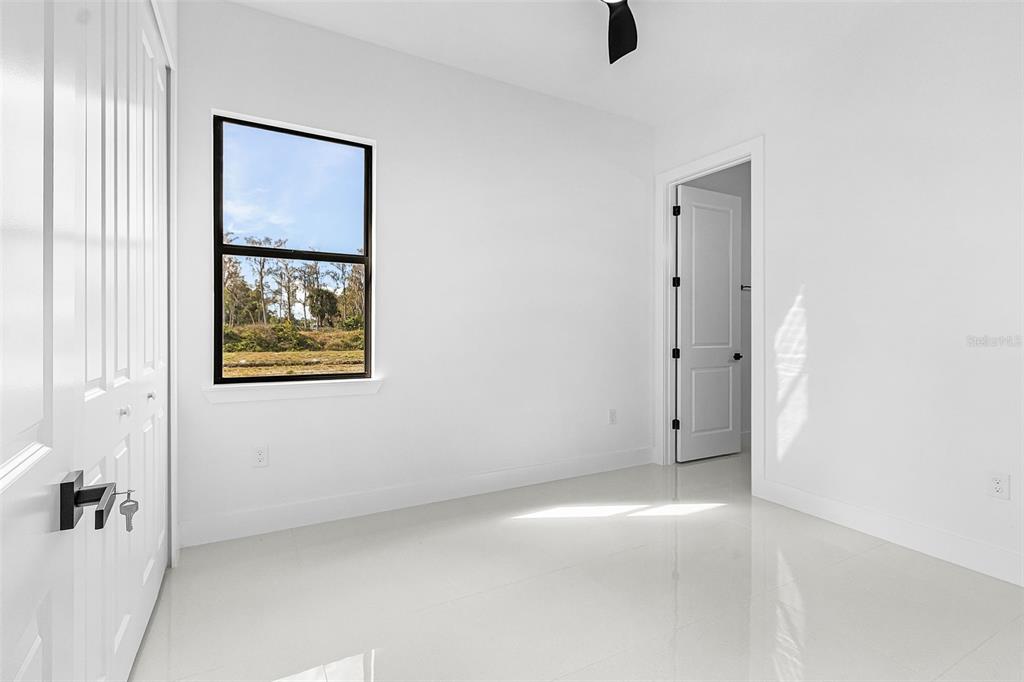 A bright, empty bedroom features white walls, glossy tile flooring, a window, and a closet — 918 ANACONDA AVENUE S, LEHIGH ACRES, FL
