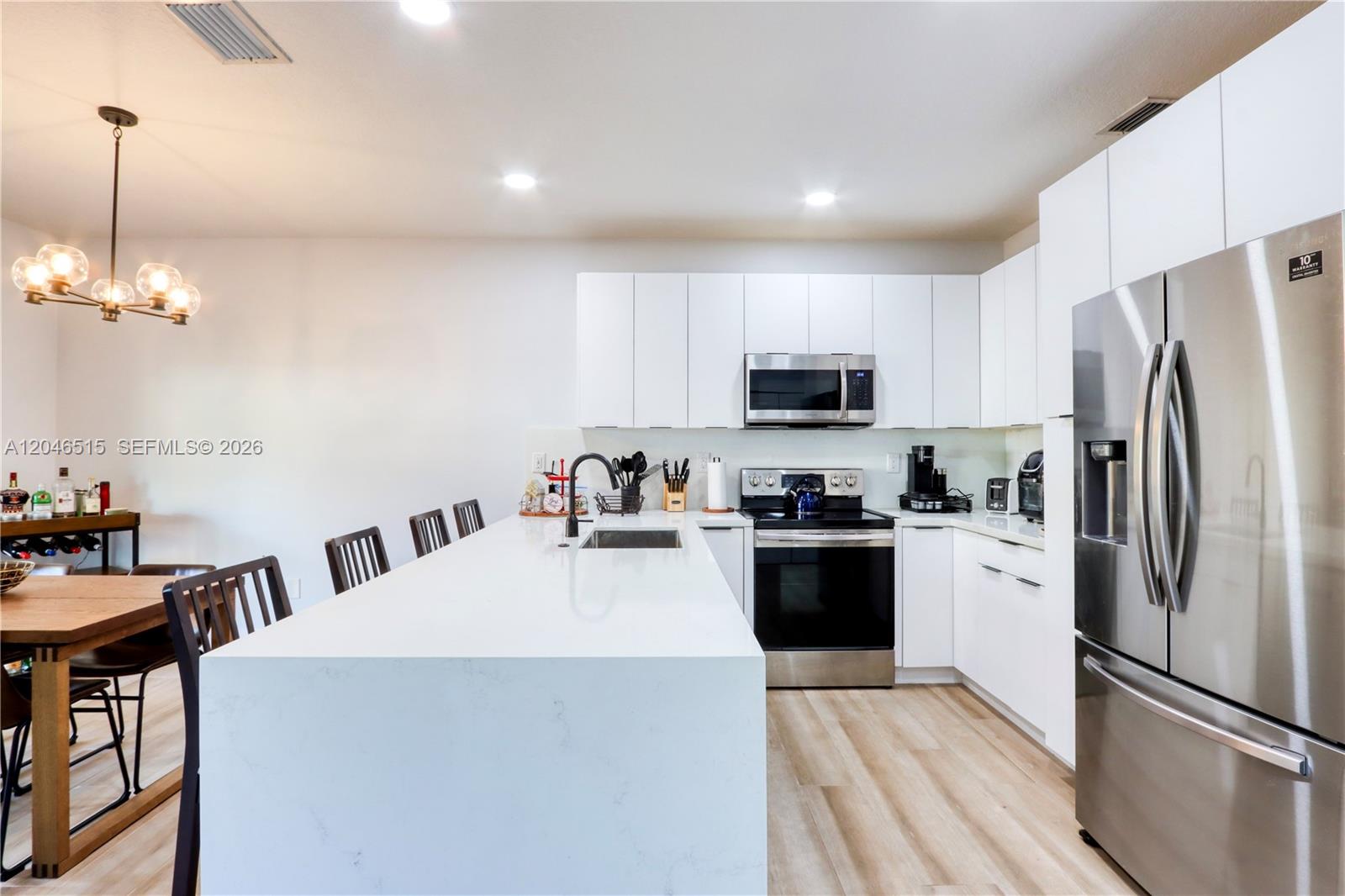 A modern kitchen features white flat-panel cabinetry, a large quartz island, and stainless steel appliances — 14302 SW 133rd Ct, Miami FL 33186, MIAMI, FL