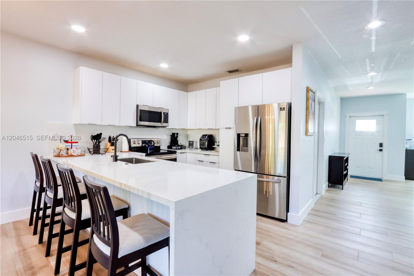 A modern kitchen features white cabinets, stainless steel appliances, and a quartz waterfall island — 14302 SW 133rd Ct, Miami FL 33186, MIAMI, FL