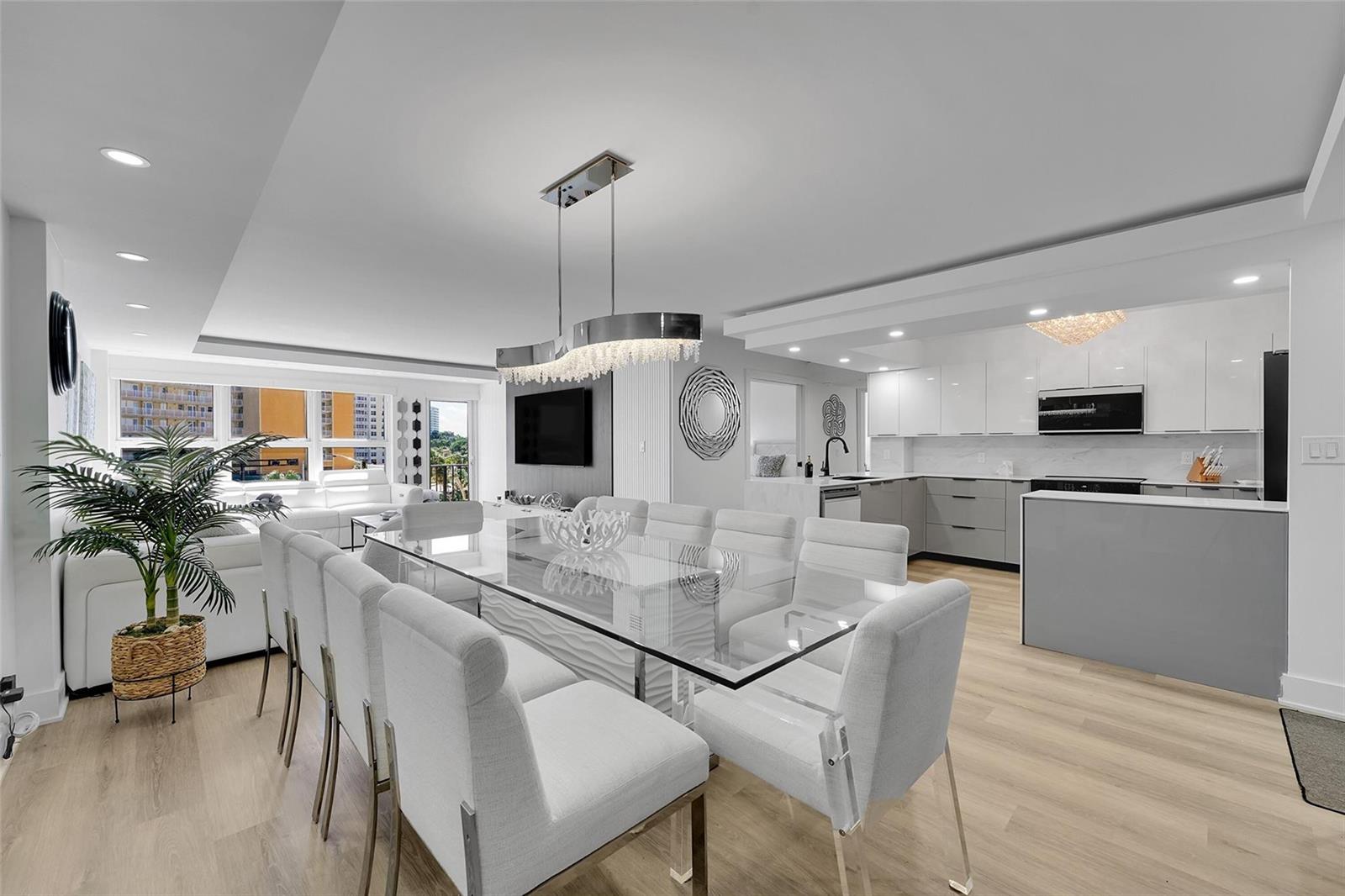 A modern dining area with a glass table and chairs sits before an open kitchen — 405 N Ocean Boulevard # 306, Pompano Beach FL 33062, POMPANO BEACH, FL