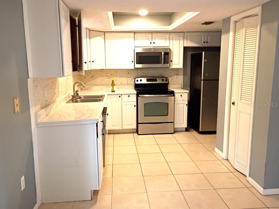 A kitchen features white cabinets, stainless steel appliances, marble-look countertops, and light tile flooring — 1208 S CANAL BOULEVARD, SEBRING, FL