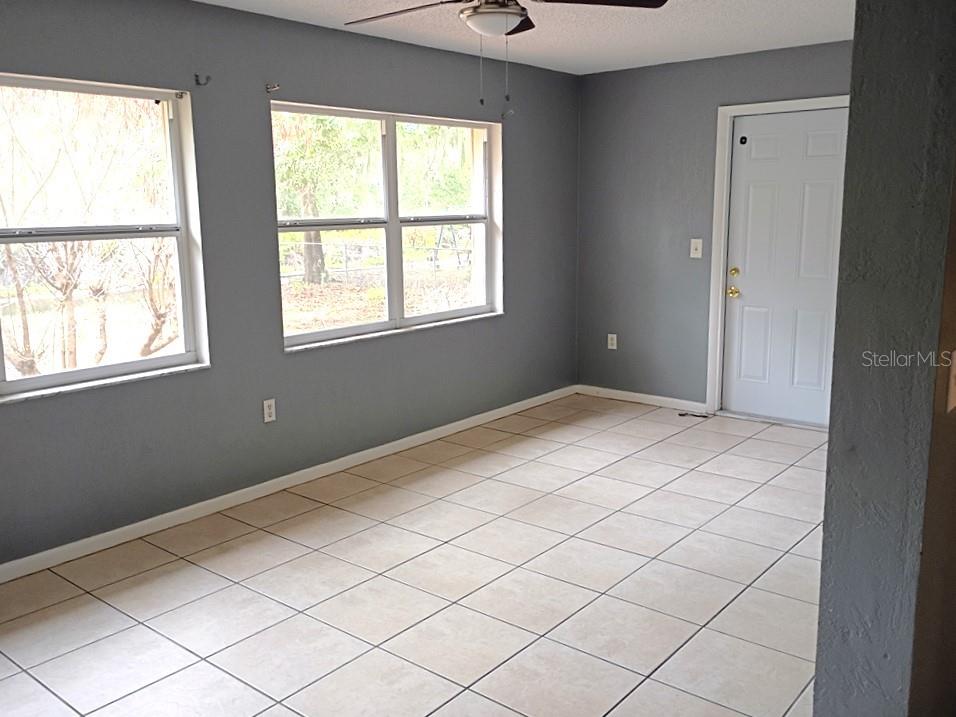A room with gray walls, tiled flooring, two windows, and a white exterior door — 1208 S CANAL BOULEVARD, SEBRING, FL